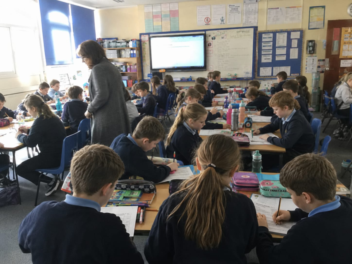 A teacher moving among a full class of pupils at work