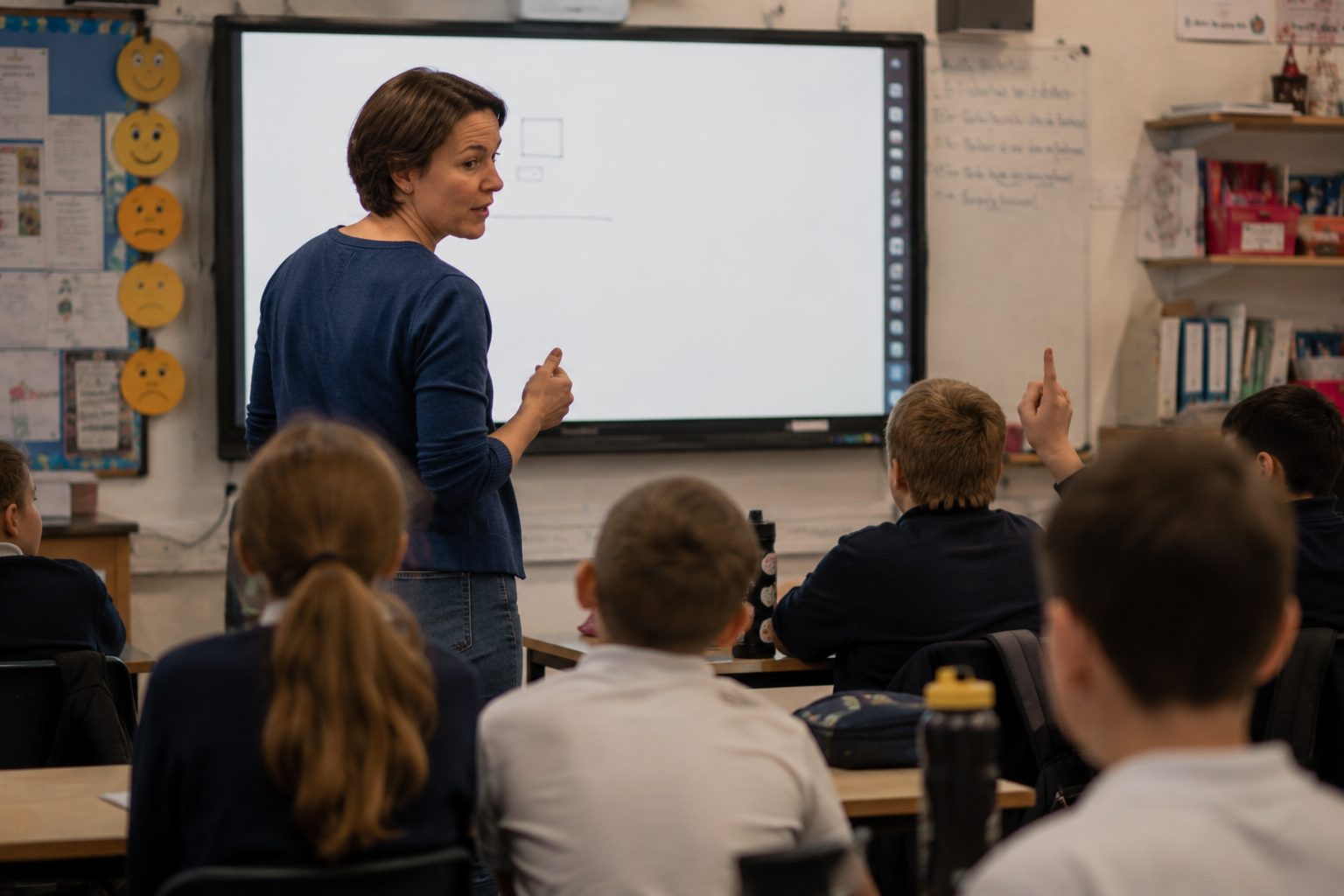 A teacher mid-lesson, turning back to a class full of raised hands
