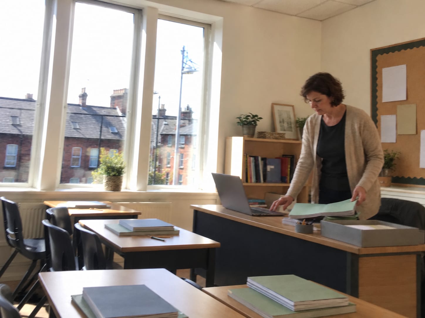 A teacher planning at her desk with a laptop and pupils' copybooks