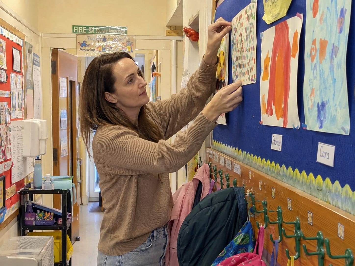 A teacher putting up a display of pupils' artwork in the classroom